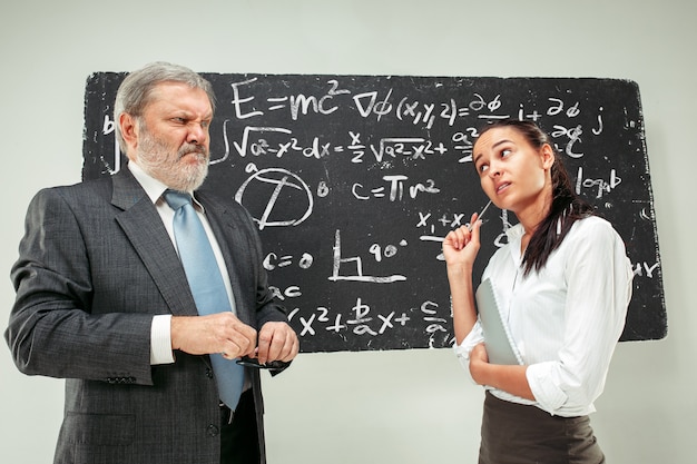 Male professor and young woman against chalkboard in classroom