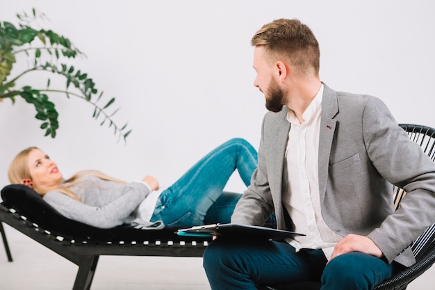 Male psychologist looking at her female patient lying on couch