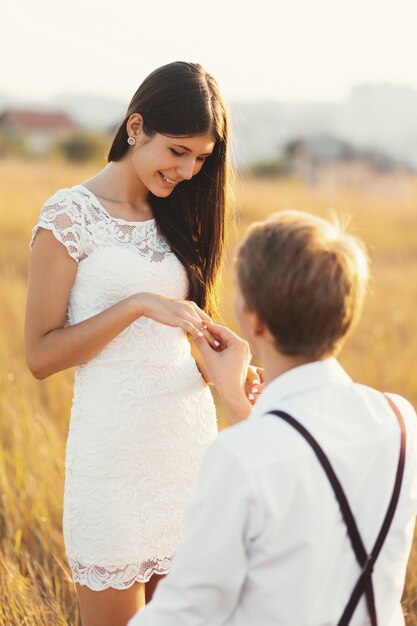 Male putting engagement ring on woman hand, outdoors in a golden