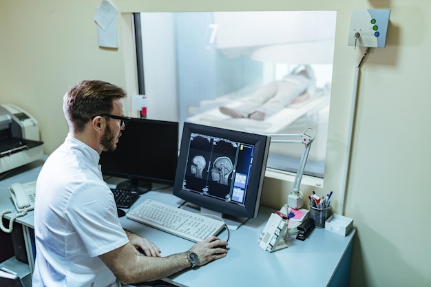 제어실에서 컴퓨터 모니터에서 환자의 MRI 스캔 결과를 분석하는 남성 방사선 전문의