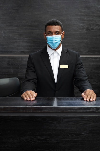 Male receptionist in suit at work wearing medical mask