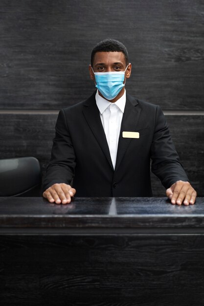Секретарь-мужчина в костюме на работе в медицинской маске