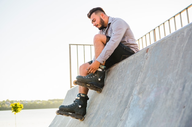 Male rollerskater putting on rollerskate in skate park