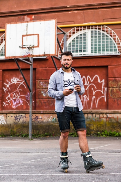 Foto gratuita rollerskater maschio facendo uso del telefono cellulare nel campo da pallacanestro