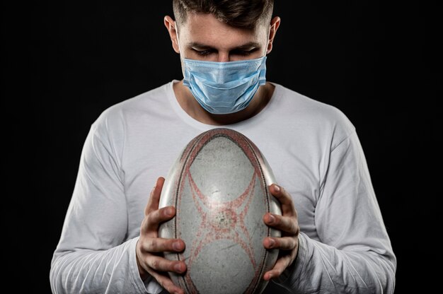 Male rugby player holding ball while wearing medical mask
