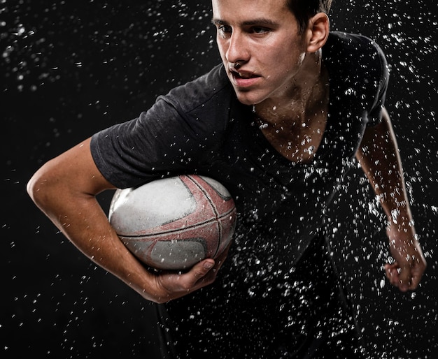 Foto gratuita giocatore di rugby maschile con palla e spruzzi d'acqua