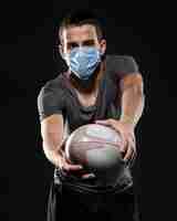 Free photo male rugby player with medical mask holding ball