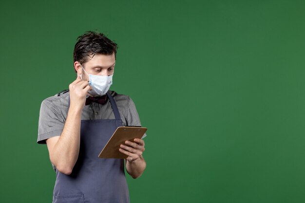 male server in uniform with medical mask and concentrated on check book pen on green background