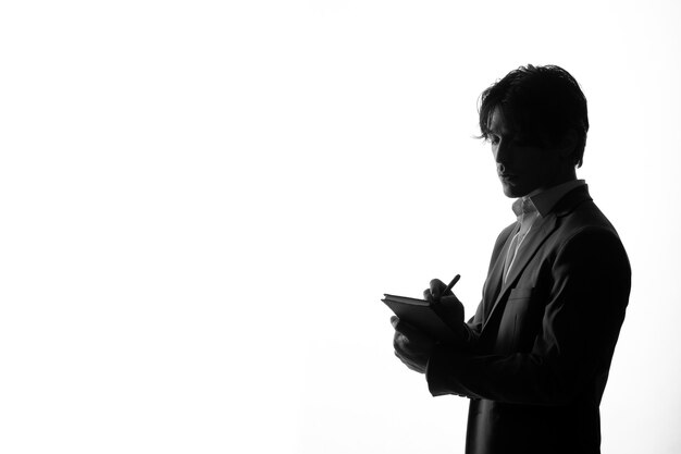 Male silhouette in strict suit taking notes side view shadow back lit white background young