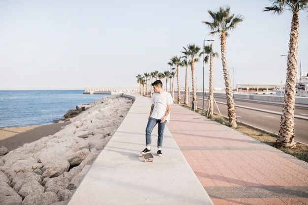 Мужской скейтбордист с скейтбордом, стоящим по морю