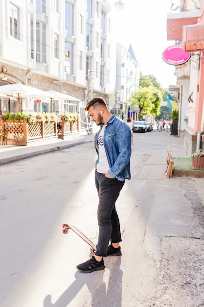 Мужской скейтбордист с скейтбордом, стоящим на улице