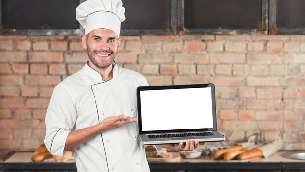 Male smiling baker showing an open laptop with blank white screen