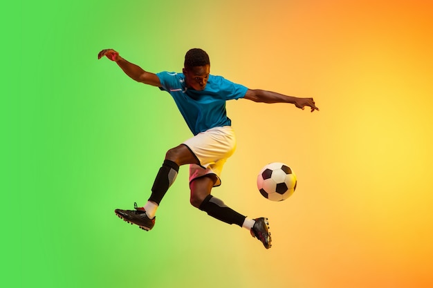 Male soccer, football player training in action isolated on gradient studio in neon light