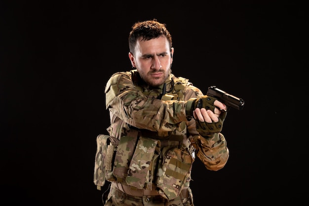Мужчина-солдат в камуфляже, направленный из пистолета на черную стену