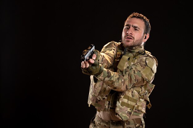 Male soldier in camouflage aiming gun on black wall