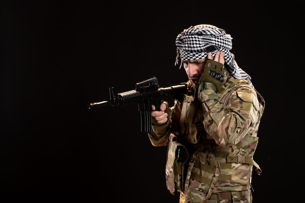 Male soldier in camouflage aiming machine gun on black wall