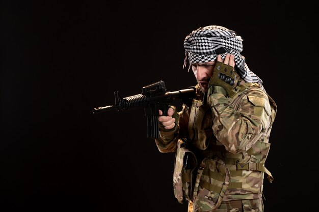 Male soldier in camouflage aiming machine gun on black wall