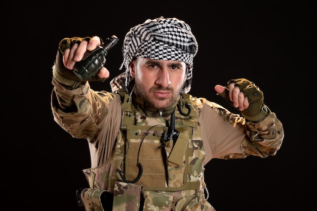 Male soldier in camouflage holding grenade on black wall