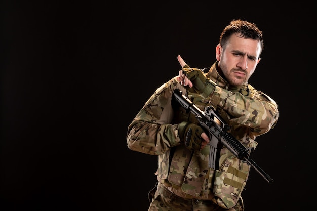 Male soldier in camouflage holding machine gun on black wall