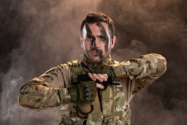 Мужчина-солдат в камуфляже перезаряжает пистолет на дымной темной стене