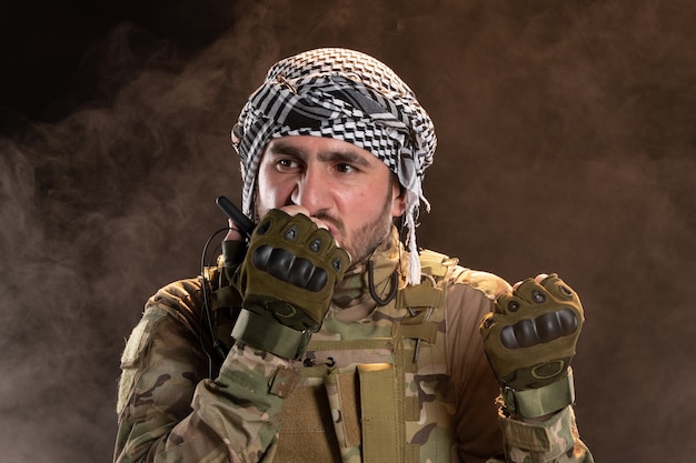 Free photo male soldier in camouflage talking through radio set on dark wall