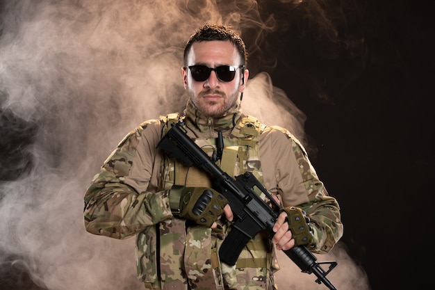 Foto gratuita soldato maschio in mimetica con mitragliatrice su carro armato guerriero scuro pavimento fumoso militare