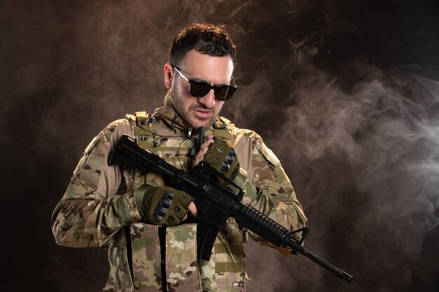 Male soldier in camouflage with machine gun on dark wall