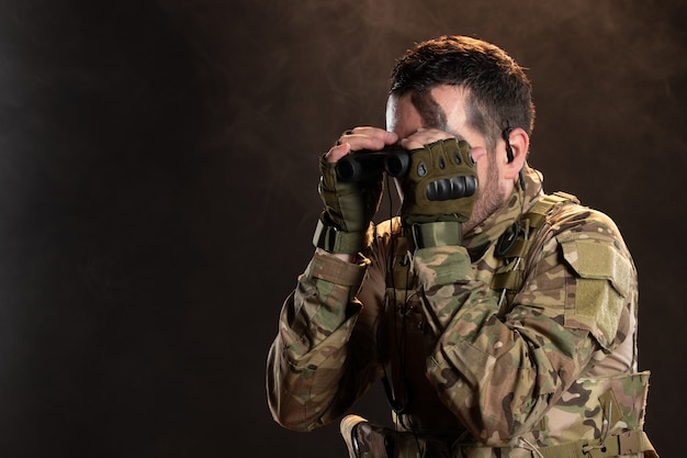 Мужчина-солдат в военной форме смотрит в бинокль на темной стене