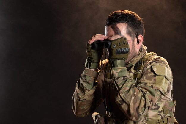 Male soldier in military uniform looking through binoculars on dark wall