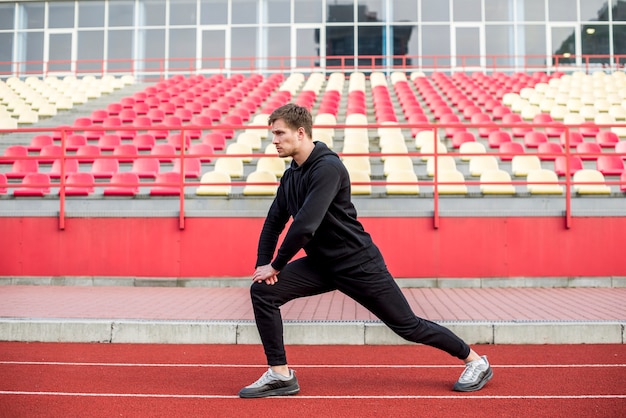 Male sportsperson exercising on race track in front of bleacher
