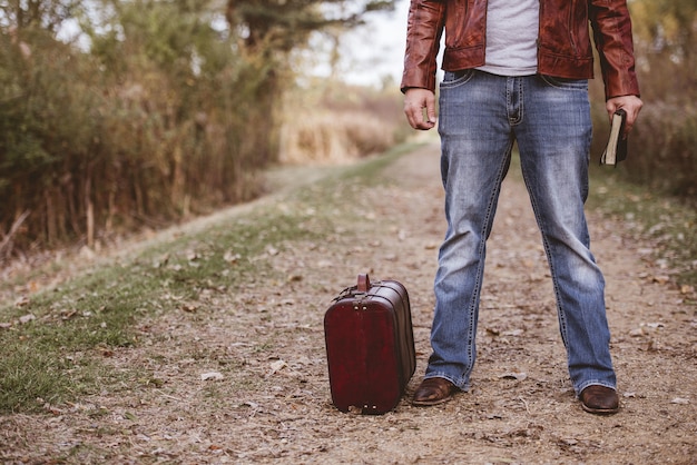 Мужчина стоял на пустой дороге возле своего старого чемодана и держа Библию с размытым фоном