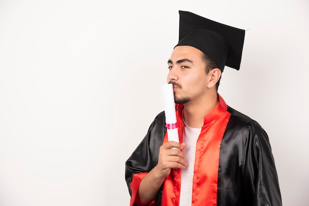 Male student kissing diploma on white.