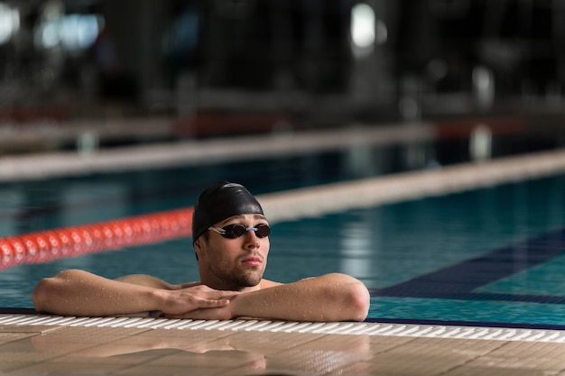 Male swimmer wearing goggles and swimming cap resting