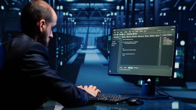 Male system engineer analyzing big data on computer, checking cloud computing network and digital servers. Young IT technician inspecting modern data center for digitalization. Handheld shot.