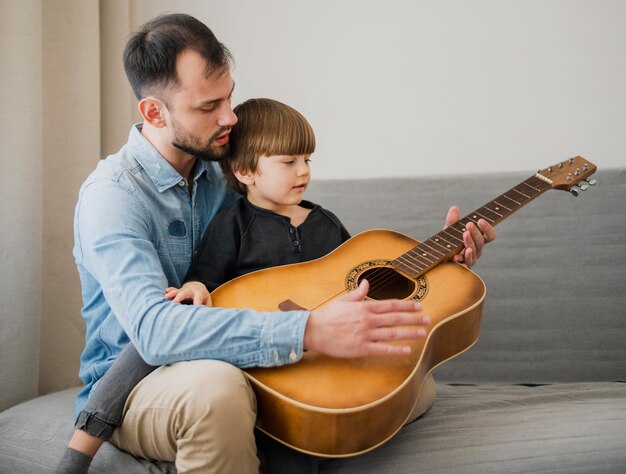 Учитель-мужчина дает уроки игры на гитаре ребенку дома