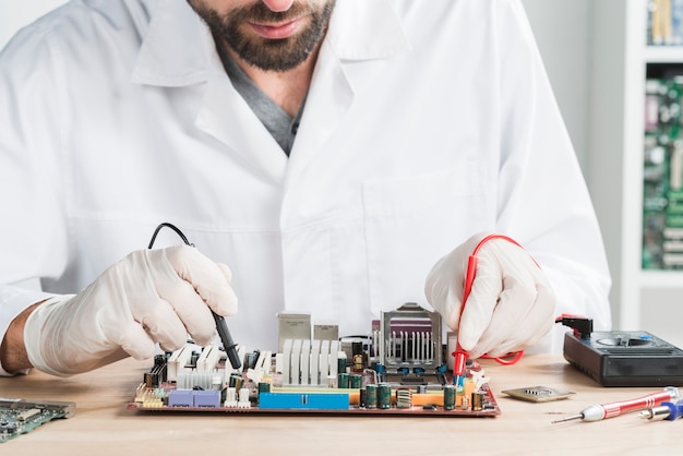 Male technician checking computer with digital multimeter on wooden desk