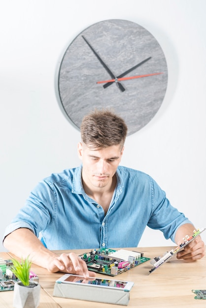 Male technician using digital tablet while repairing motherboard