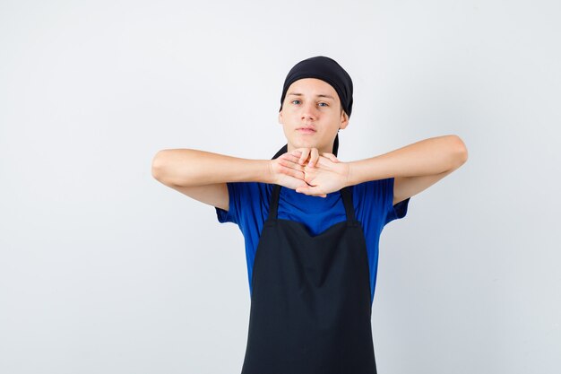 Male teen cook stretching arms in t-shirt, apron and looking tired. front view.