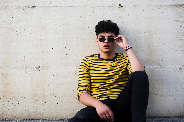 Male teenager sitting on ground and leaning on concrete wall