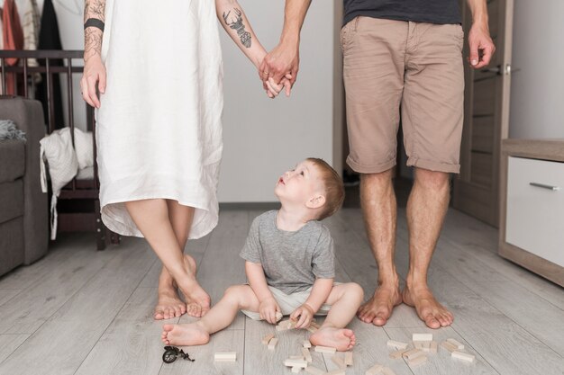 Male toddler playing with wooden blocks looking at couple holding each other's hand