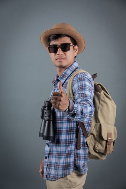 Male tourists backpacking holding binoculars gray background.