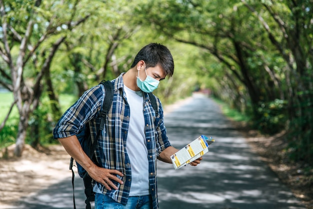 Male tourists stand and look at the map on the road.