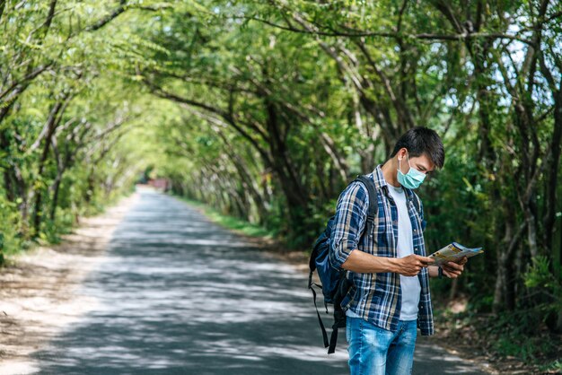 Male tourists stand and look at the map on the road.