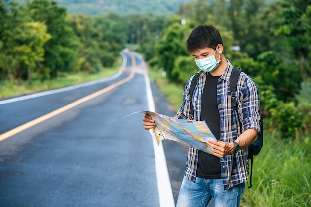 Male tourists stand and look at the map on the road.