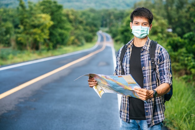 Male tourists stand and look at the map on the road.