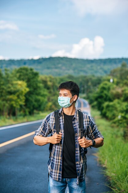 Male tourists wearing a mask, carrying a backpack on the road.