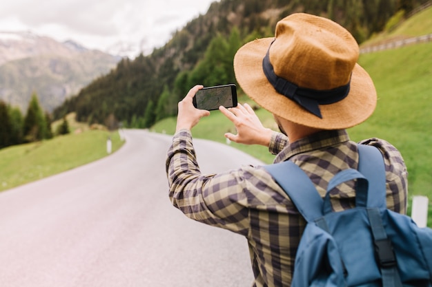 Male traveler in brown hat searching right road by using online map standing on beautiful mountain