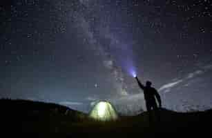 Free photo male traveler shining flashlight into night starry sky