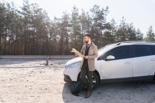 Мужской путешественник, стоя возле своей роскошной машине, держа карту в руке, глядя