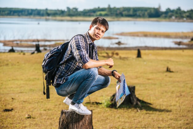 A male traveler with a backpack carrying a map and sitting on a tree stump.